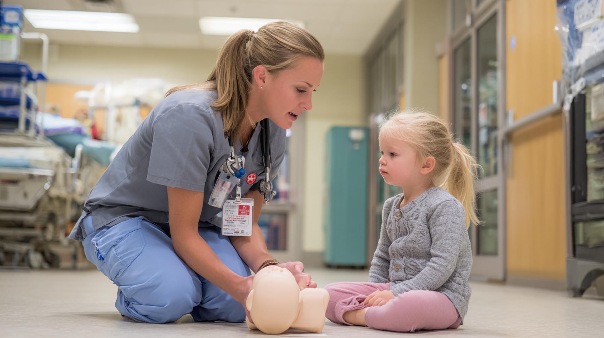 A nurse uses a doll to explain a procedure, demonstrating the age-appropriate communication taught in this pediatric emergency CE Nursing course.
